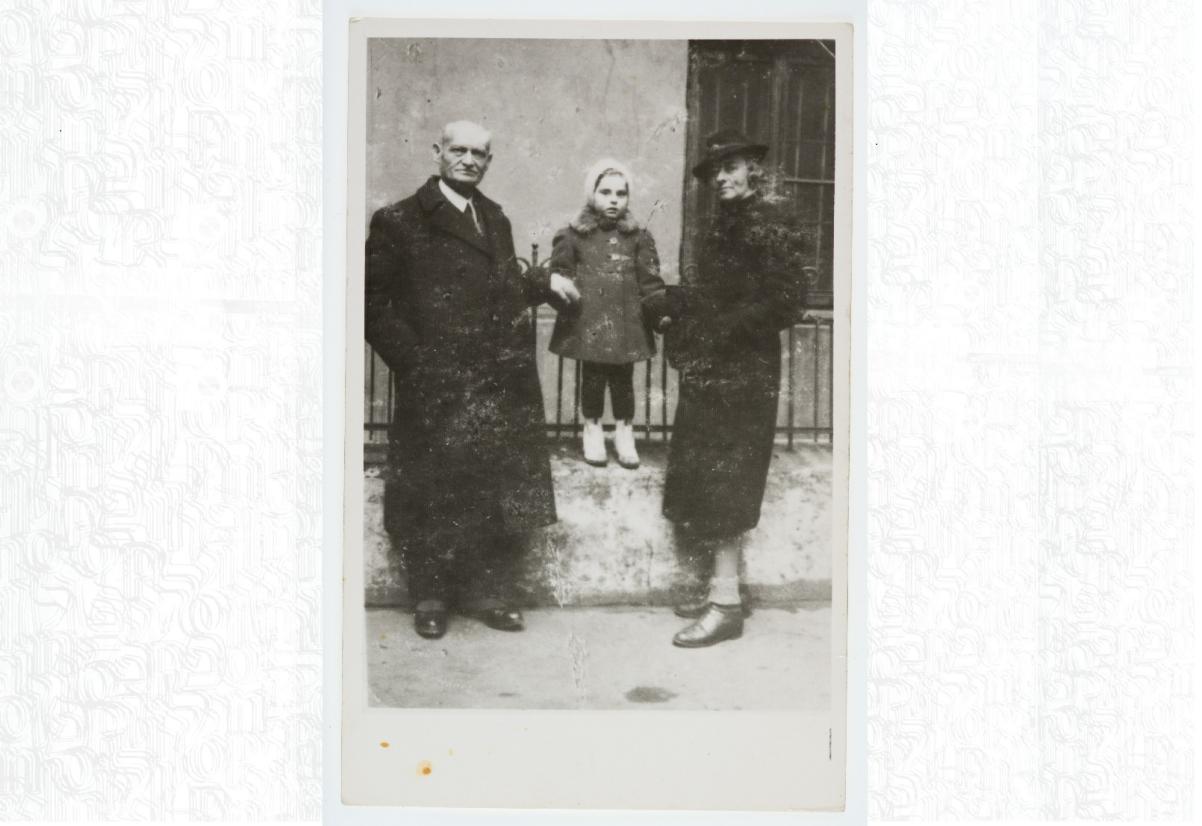 Mała Aleksandra Rozengarten (obecnie Kaniuka) stoi na ogrodzeniu. Za ręce trzymają ją matka Irena i dziadek Eliezer Rozengarten. / Aleksandra Rozengarten is standing on a fence, her mother Irena and grandfather Eliezer Rozengarten holding her hands.