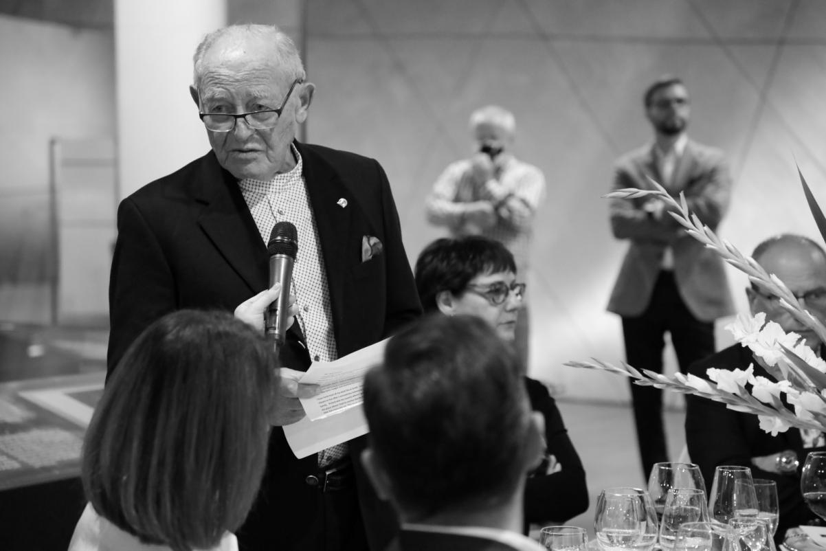 Spotkanie w Muzeum POLIN - Nimrod S. Ariav przemawia przez mikrofon. Przy stoliku siedzą inni goście.