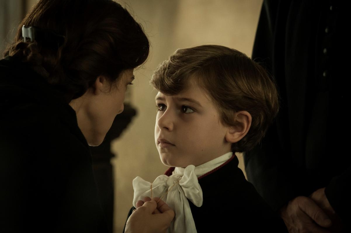 Kadr z filmu "Porwany" - kobieta łapie za łańcuszek wiszący na szyi małego odświętnie ubranego chłopca.