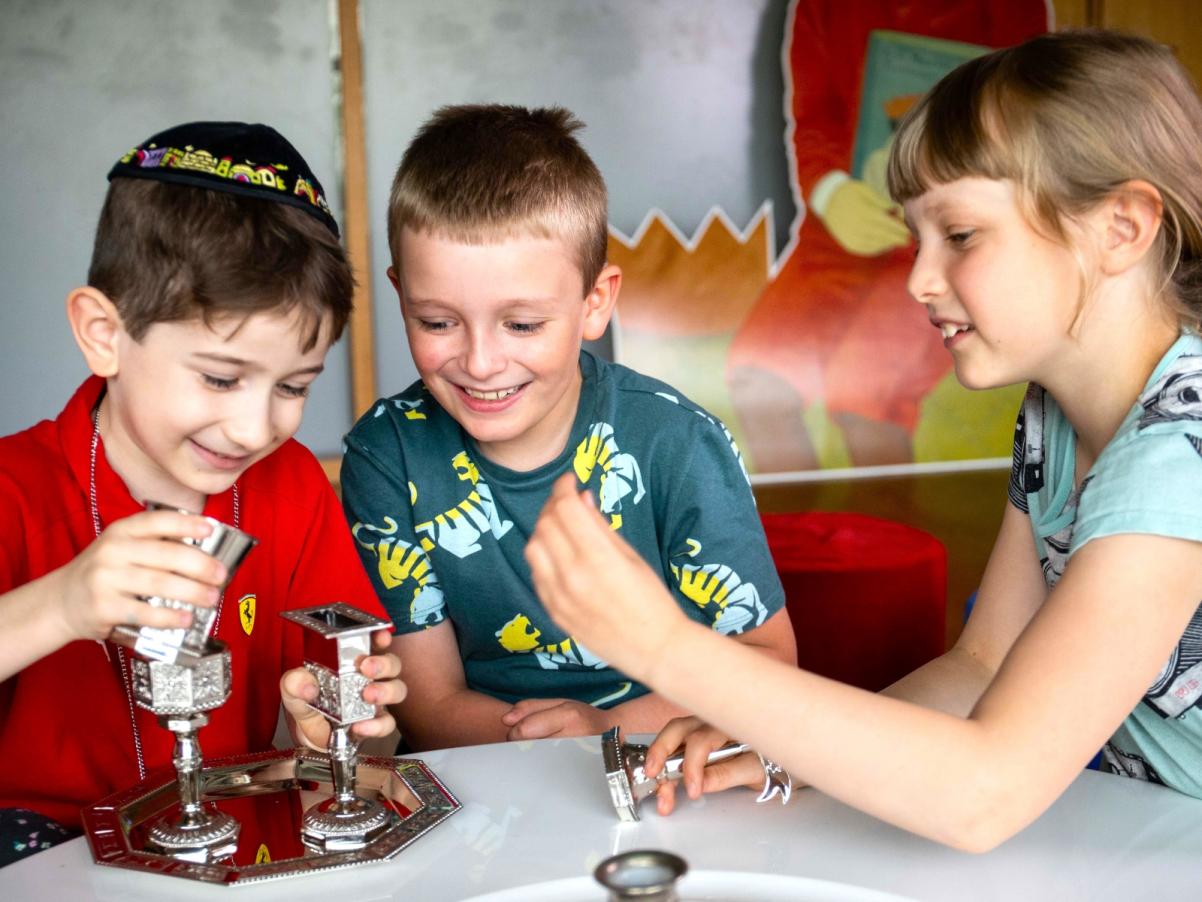 Dwaj chłopcy i jedna dziewczynka bawią się srebrnymi kielichami w Miejscu edukacji rodzinnej "U króla Maciusia".