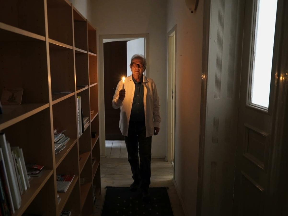 Kadr z filmu "Zamek mojego ojca". Starszy mężczyzna idzie ze świecą przez korytarz.