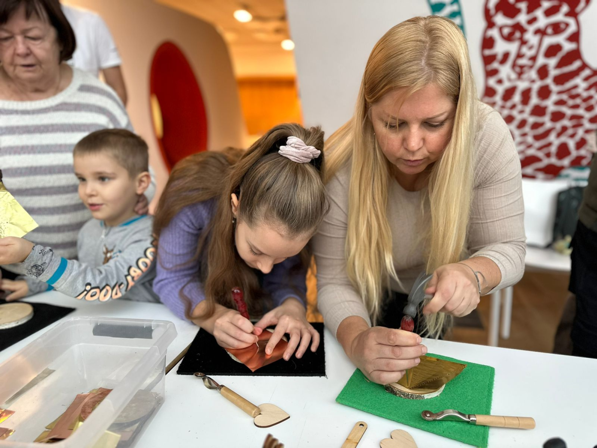 Miejsce edukacji rodzinnej. Dwie kobiety przygotowują prace plastyczne z dziećmi - jedna z chłopcem, druga z dziewczynką.