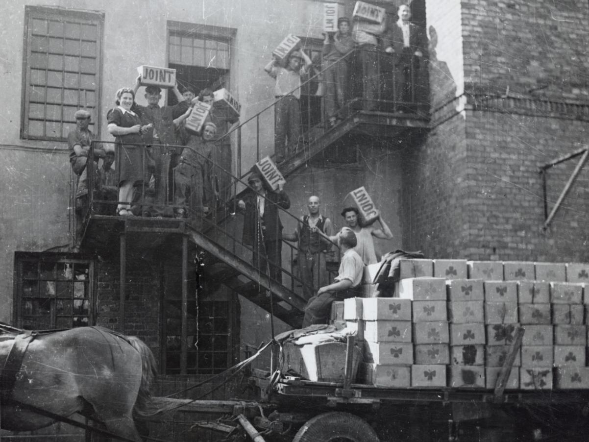 Supplies being taken off a horse-drawn wagon and being carried into a warehouse in Warsaw; the crates are labeled "JOINT".