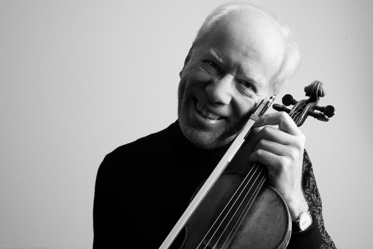 Gidon Kremer - na zdjęciu widzimy Kremera uśmiechniętego, ze skrzypcami przy policzku. Zdjęcie czarno-białe.