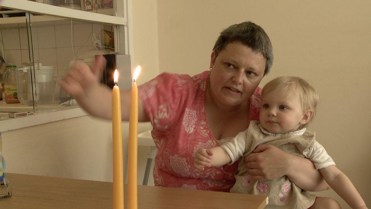 Kobieta trzyma dziecko na rękach, wskazuje mu dłonią zapalone świece.