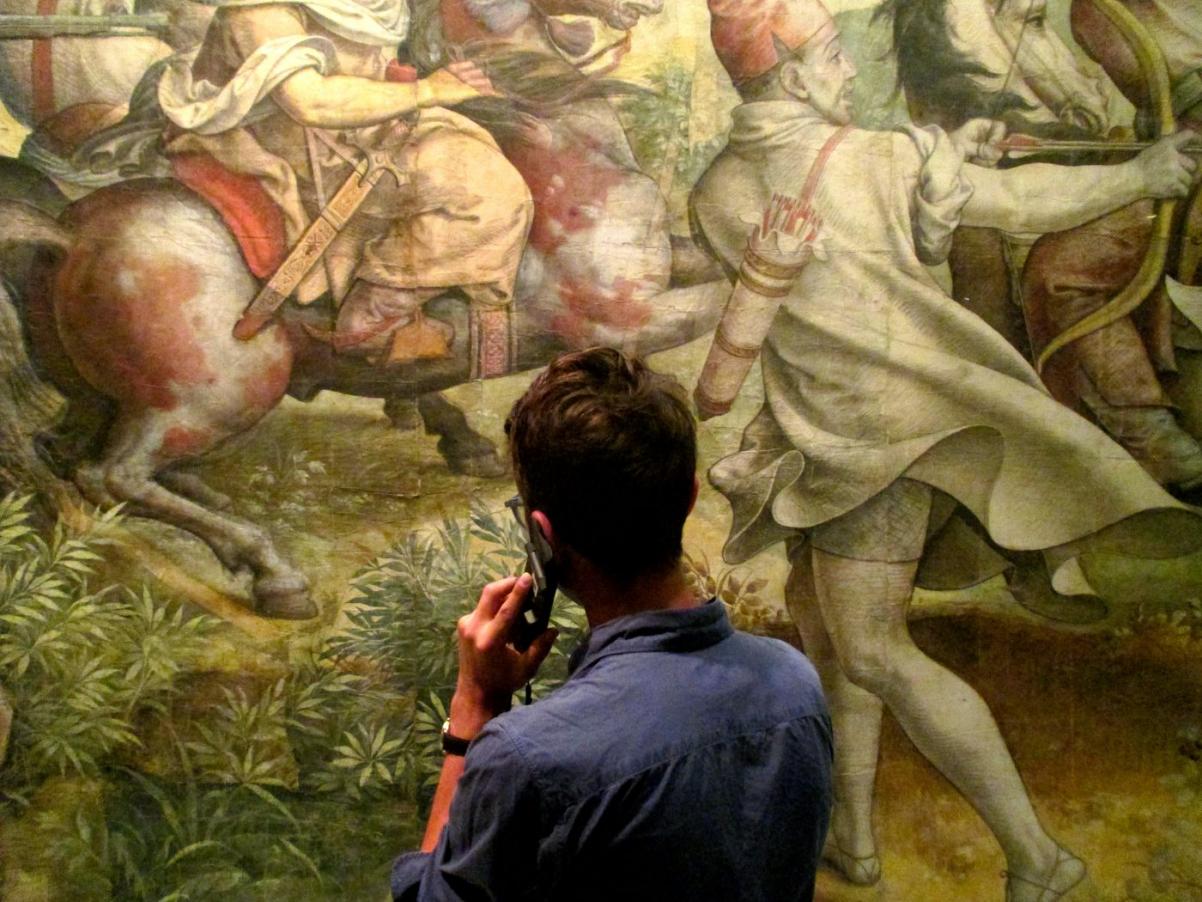 Zwiedzający ogląda obraz w muzeum. Do ucha przykłada audioprzewodnik.