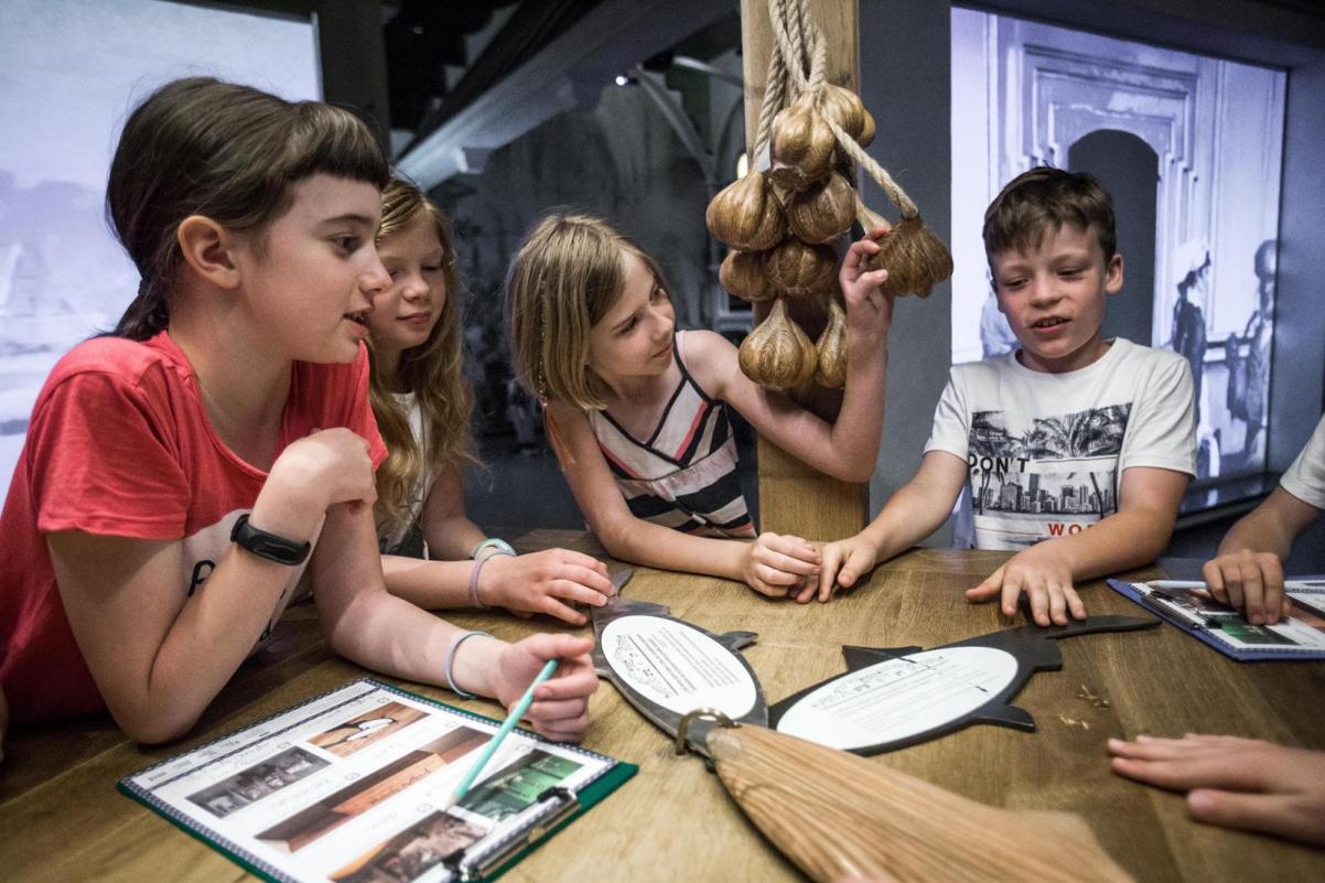 Zdjęcie ilustracyjne. Przedstawia grupę dzieci na zajęciach edukacyjnych na wystawie w muzeum