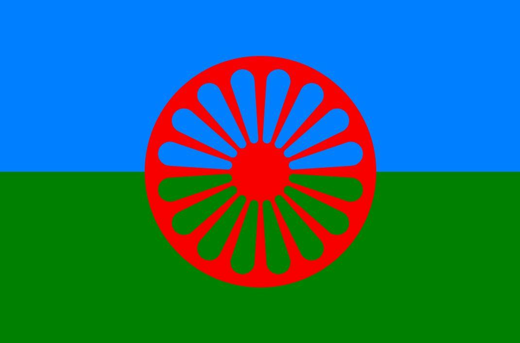 Symbol narodowy Romów. Flaga niebiesko-zielona, na środku czerwone koło zębate, Dharmaćakra.