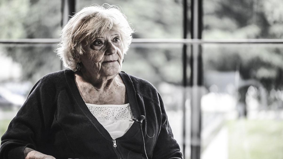 Starsza kobieta w ciemnym sweterku pozuje na tla okna