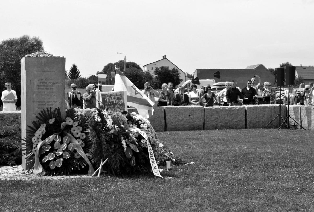 Czarno-białe zdjęcie. Kwiaty leżą pod pomnikiem.
