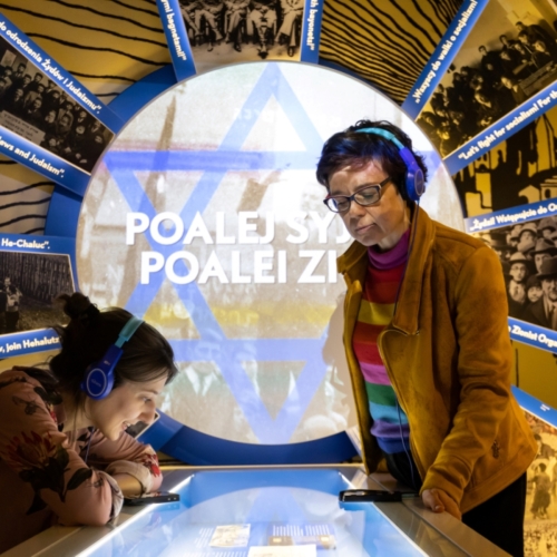 Dwie kobiety ze słuchawkami na uszach zwiedzają wystawę stałą w Muzeum POLIN.