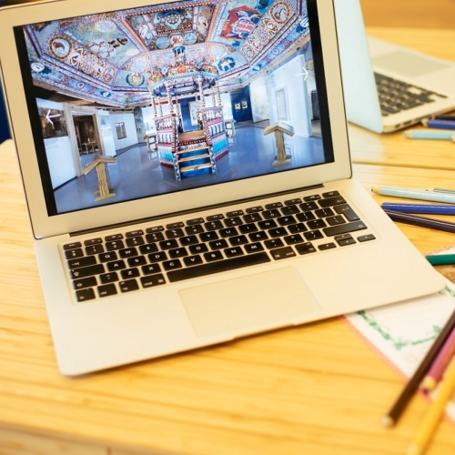 Na biurku rozrzucone kolorowe kartki i ołówki. Otwarty laptop, na którego ekranie widać rekonstrukcję dachu synagogi z Gwoźdźca.