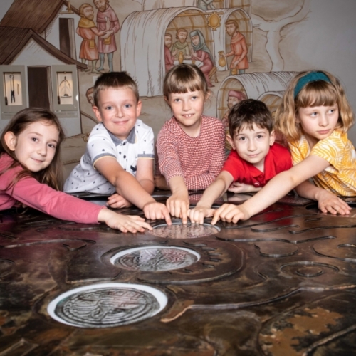 Pięcioro dzieci dotyka gabloty z monetami prezentowanej na wystawie stałej w Muzeum POLIN.