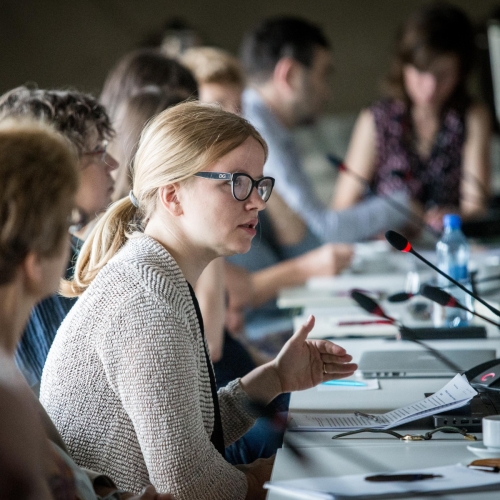 Uczestniczki i uczestnicy konferencji naukowej siedzą przy stole, przy mikrofonach.