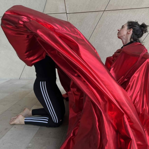 Two women wrapped in red fabric sit in the main hall of the POLIN Museum.