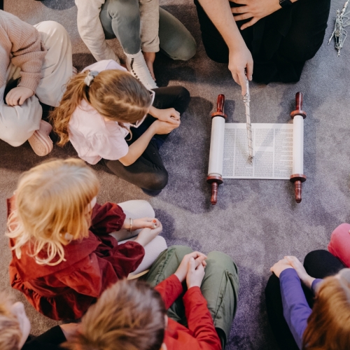 Someone is holding the Torah scroll. Children are sitting around it.
