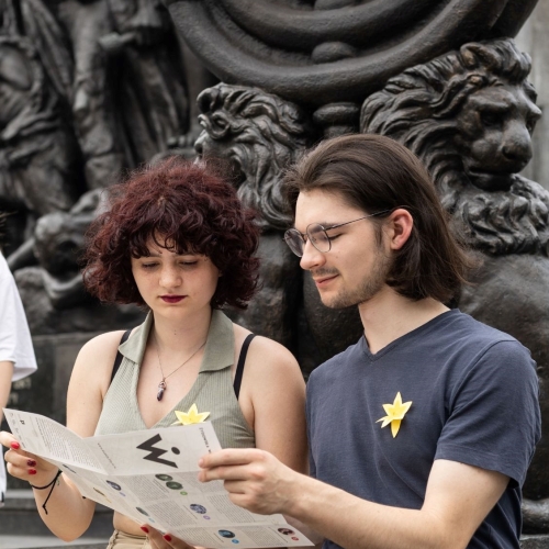 Nastolatki przy Pomniku Bohaterów Getta. Dwoje z nich ogląda jakąś broszurę. Obok nich stoi dziewczyna.