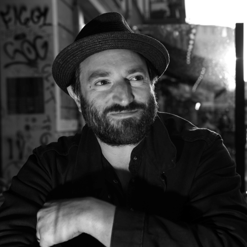 Daniel Kahn w kapeluszu. W tle ulica w Berlinie.