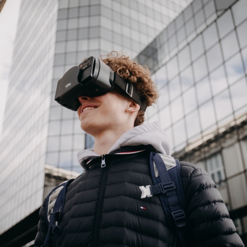 Nastolatek ma na głowie gogle VR. W tle Błękitny Wieżowiec na placu Bankowym w Warszawie.